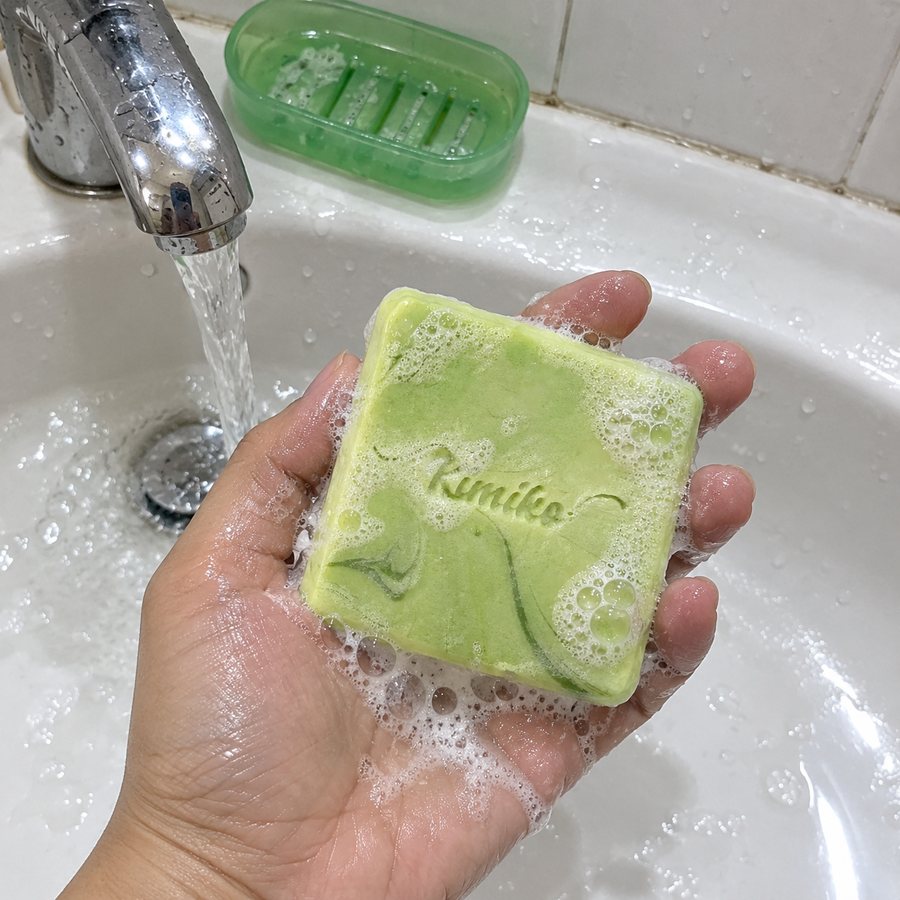 A wet hand holding the lathered green KIMIKO tawas bar over the sink